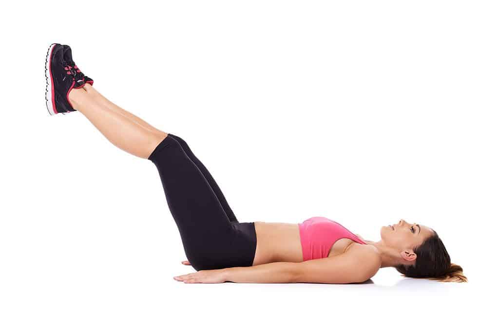 Woman doing leg lifts to strengthen her abdominal muscles while lying on the floor working out, studio portrait over white
