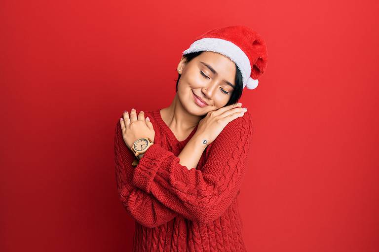 Beautiful young woman with short hair wearing christmas hat hugging oneself happy and positive, smiling confident. self love and self care