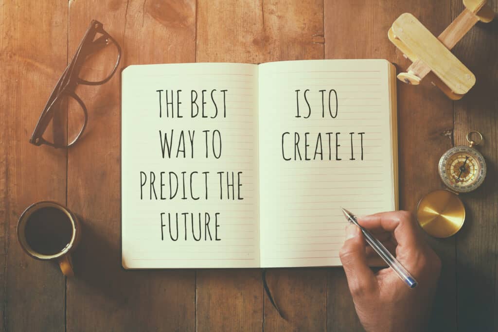 open notebook over wooden table with motivational saying the best way to predict the future is to create it