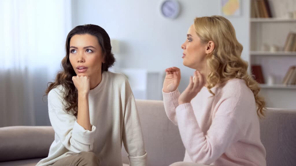 Young lady getting bored about conversation with her friend, fake relationship