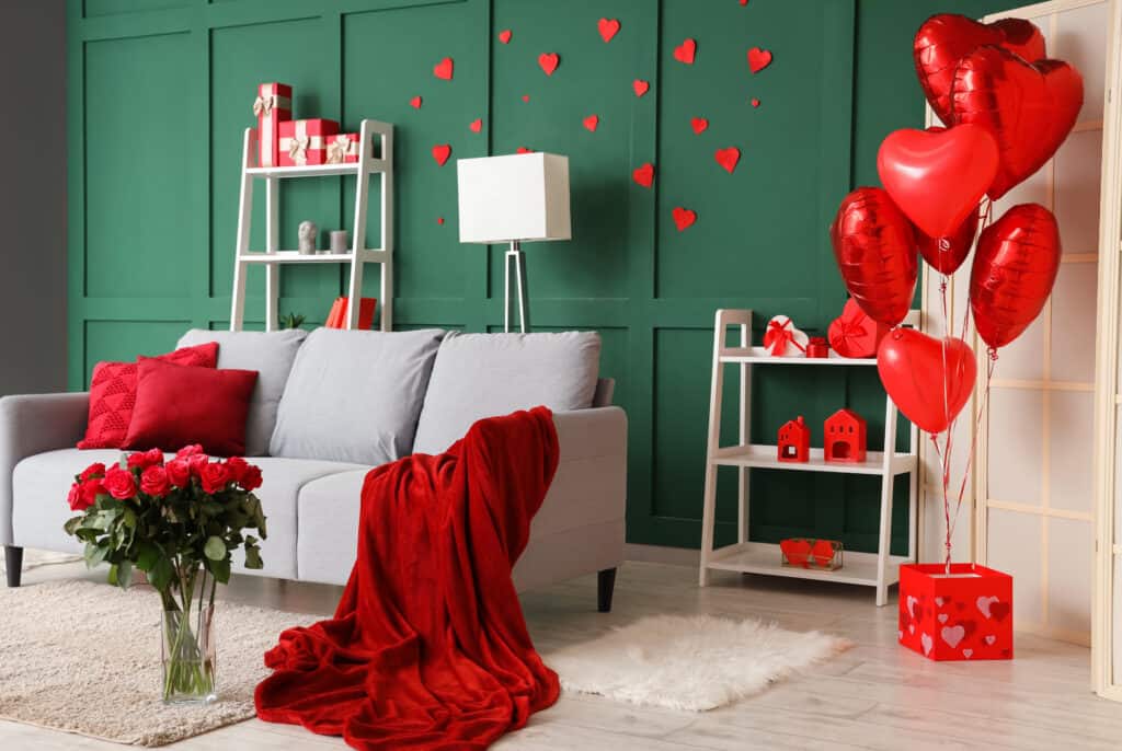 Interior of festive living room with grey sofa, bouquet of roses and heart-shaped balloons. Valentine's Day celebration